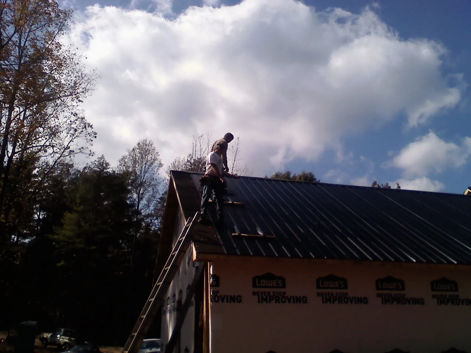 Roofer fastening dark metal panels high against a cloudy sky, from a Roof Inspection job in Saluda