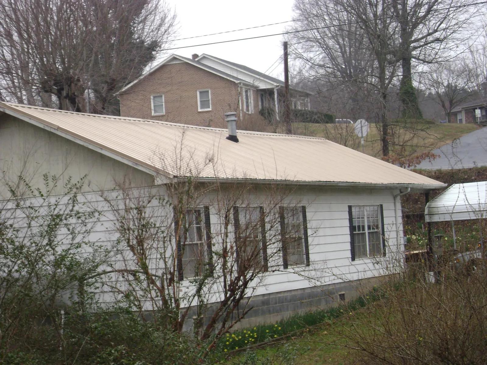 Tan metal roof on a white sided house set into a hillside — Commercial Roofing by Roofing Brothers in Saluda