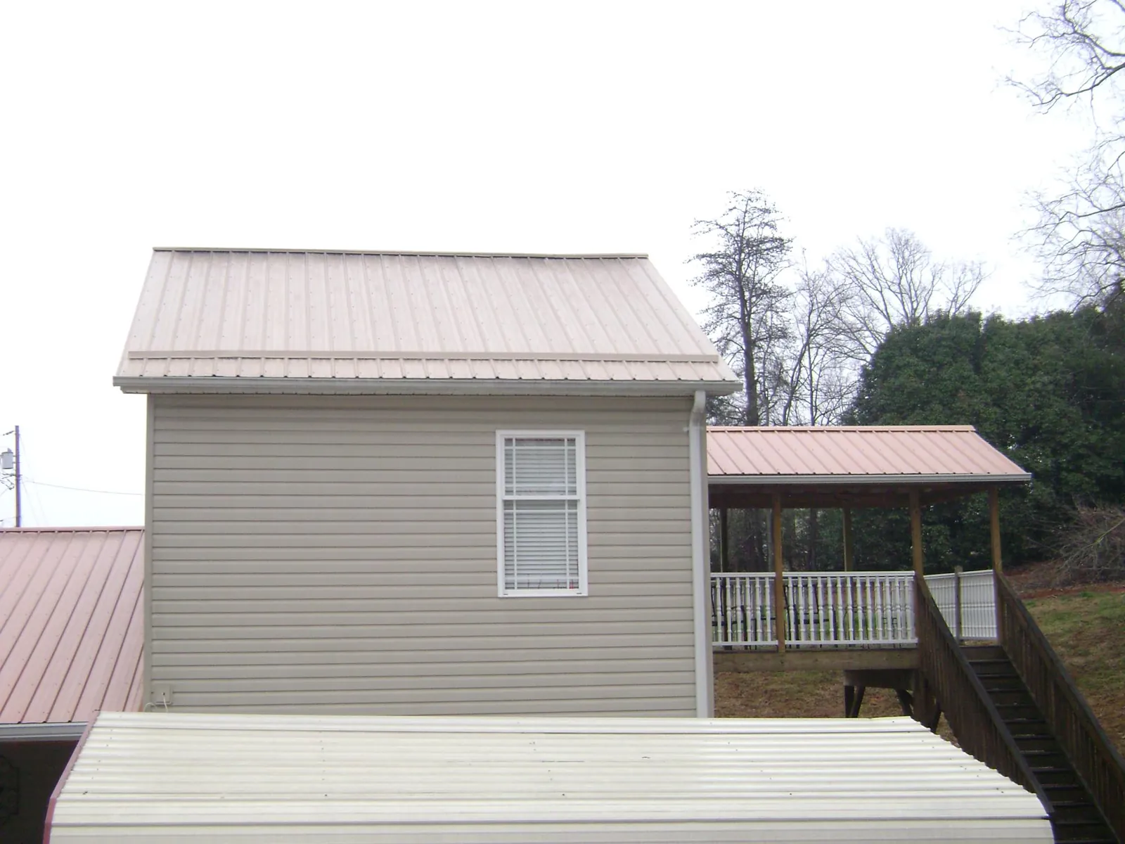 Tan metal roofs on a two story addition and attached porch, from a Roof Replacement job in Saluda